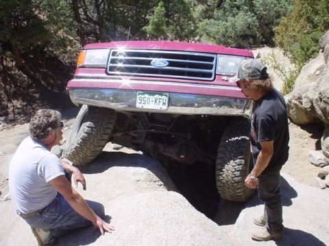 1991 Ford Bronco - A red 1991 Ford Bronco is shown navigating a difficult rocky path with two people observing.