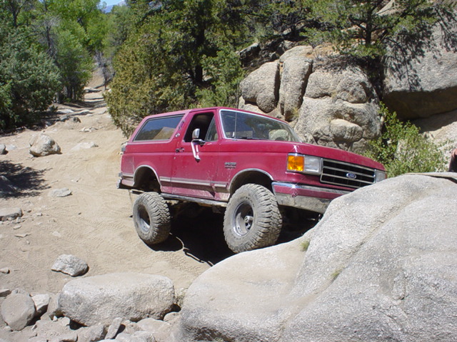 Red 1991 Ford Bronco climbing over rocks on a dirt trail