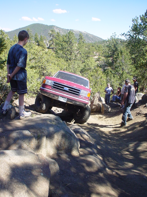 1991 Ford Bronco - A red Ford Bronco navigates a rocky off-road trail with onlookers.