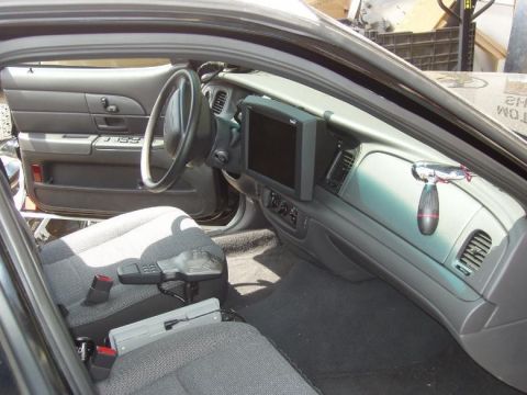 2000 Ford Crown Victoria - The interior of a 2000 Ford Crown Victoria police car is visible, a mounted screen on the dashboard and police equipment.