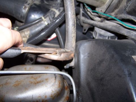 1986 Ford Bronco - Close-up of a hand using pliers on a metal component within an engine compartment.