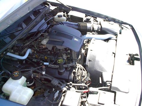 1985 Mercury Grand Marquis - The engine bay of a vehicle, a V8 engine with its cover and air intake system visible.