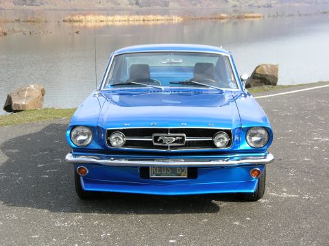 1965 Ford Mustang - A blue 1965 Ford Mustang is parked in front of a body of water.