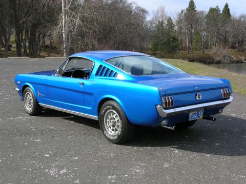 1965 Ford Mustang - This blue 1965 Ford Mustang fastback coupe is shown from the rear 3/4 angle, with its license plate clearly visible.