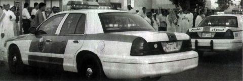 1999 Mercury Grand Marquis - Two police cars are parked side-by-side, with a crowd of people gathered in the background.