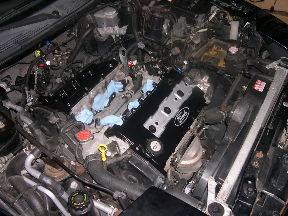 Close-up of a Ford engine with black valve covers and blue rags stuffed into openings. Radiator and hoses visible