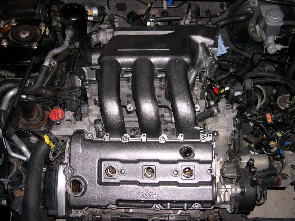 Engine with black intake manifold and Ford-branded valve cover. Wires and hoses are visible