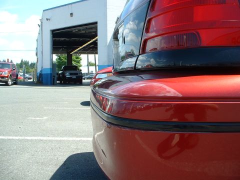 1999 Ford Crown Victoria - Rear view of a red 1999 Ford Crown Victoria showing damage to the bumper. The vehicle is parked outside a service bay.