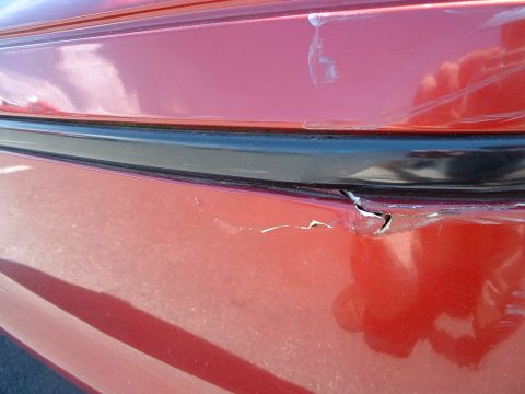 1999 Ford Crown Victoria - This photo shows damage to a red vehicle's rear bumper area, with visible scrapes and a crack in the plastic.