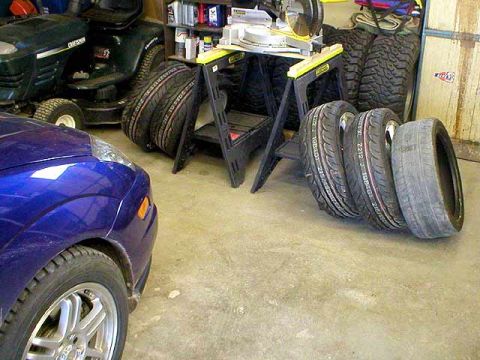2004 Ford Focus - A blue car's front fender and wheel are visible next to a stack of tires in a garage.