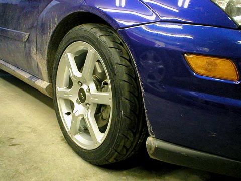 2004 Ford Focus - The wheel and fender of a blue car are shown, with the SVT logo visible on the wheel hub.