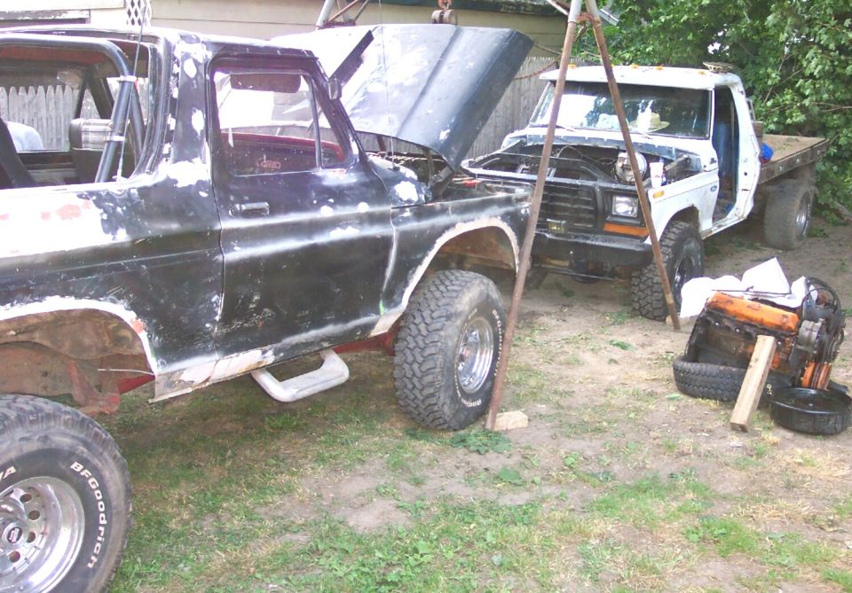 Stripped black Ford truck beside a white Ford flatbed during an engine swap