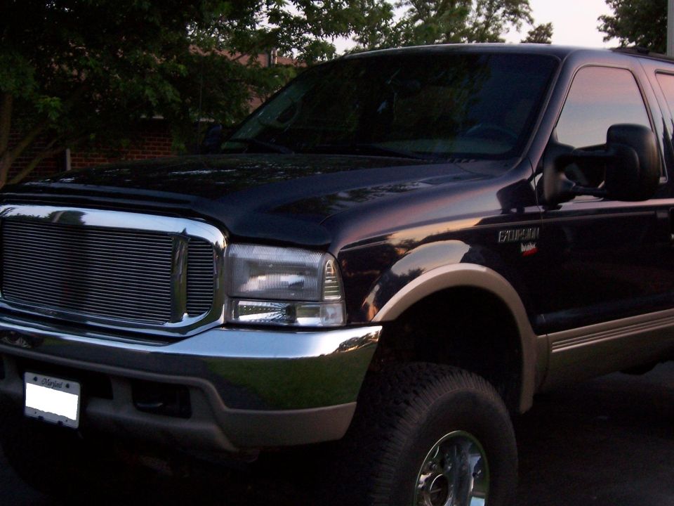 Black Ford Excursion front three-quarter with chrome billet grille and lift, parked by brick wall