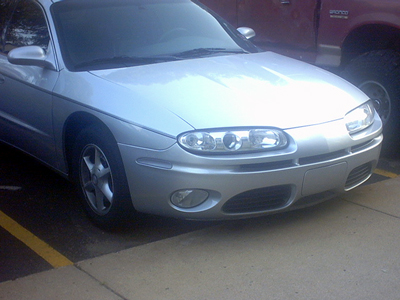 2002 Oldsmobile Aurora - Front view of a silver 2002 Oldsmobile Aurora parked next to a red truck.