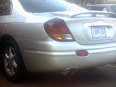 2002 Oldsmobile Aurora - The rear of a silver sedan is shown, a spoiler and dual exhaust pipes.