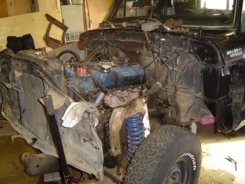 1979 Ford Bronco - A black square-body Ford 4x4 sits torn down in a garage with the front fenders, grille and hood removed, exposing a blue Ford V8, loose eng…