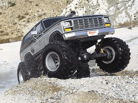1994 Ford Bronco - This lifted truck navigates a rocky, watery terrain with its massive tires kicking up spray.