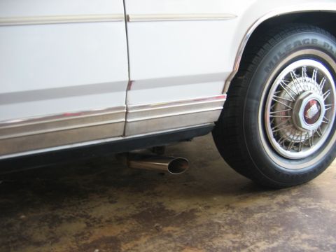 1985 Ford LTD Crown Victoria - Close-up of a chrome exhaust pipe extending from the underside of a white vehicle.