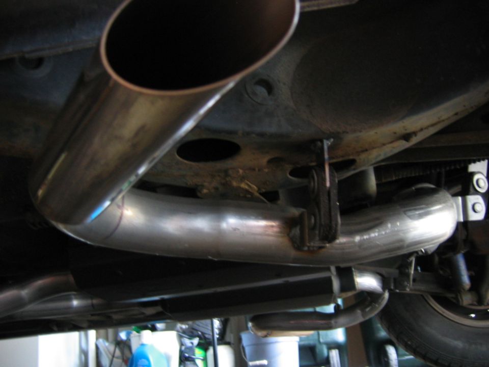 Exhaust pipe system under a vehicle, showing a curved metal pipe and hangers
