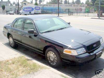 2003 Ford Crown Victoria - A black Ford Crown Victoria is parked curbside on a sunny day, with a delivery truck and building in the background.