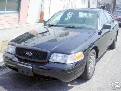 2003 Ford Crown Victoria - A black Ford Crown Victoria is parked on the side of the road with a building in the background.