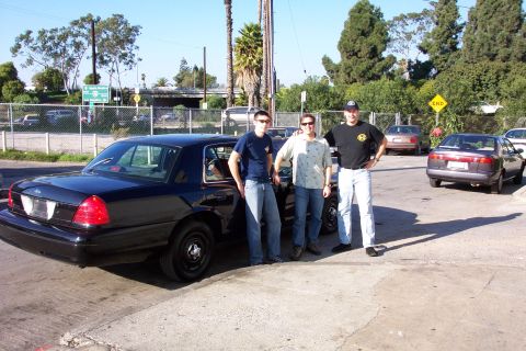 2003 Ford Crown Victoria - Three men pose with a black Ford Crown Victoria, with another vehicle visible in the background.