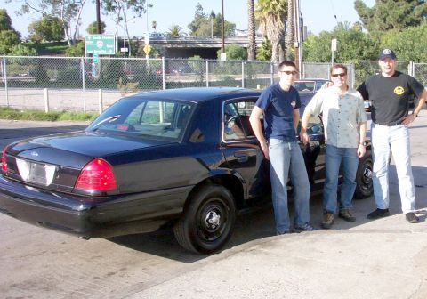 2003 Ford Crown Victoria - A dark 2003 Ford Crown Victoria is shown from the rear quarter with three men standing next to it.