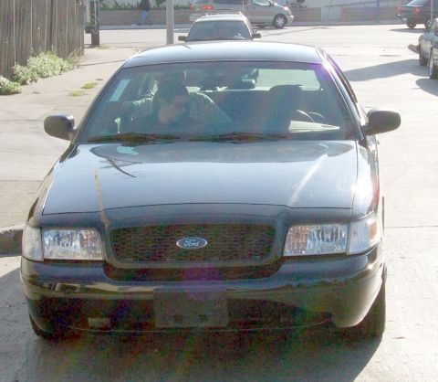 2003 Ford Crown Victoria - A black 2003 Ford Crown Victoria is parked on a street with two occupants visible inside.