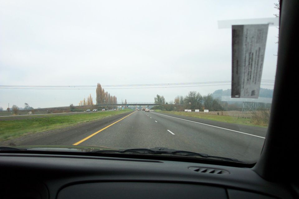 View from inside a car looking out at a highway with other cars visible in the distance and a sticker on the windshield
