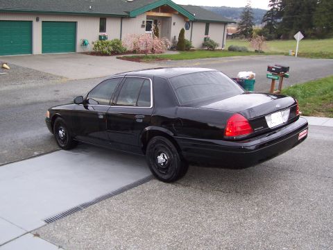 2003 Ford Crown Victoria - A black 2003 Ford Crown Victoria is parked on a driveway, angled away from the camera, with a suburban house in the background.