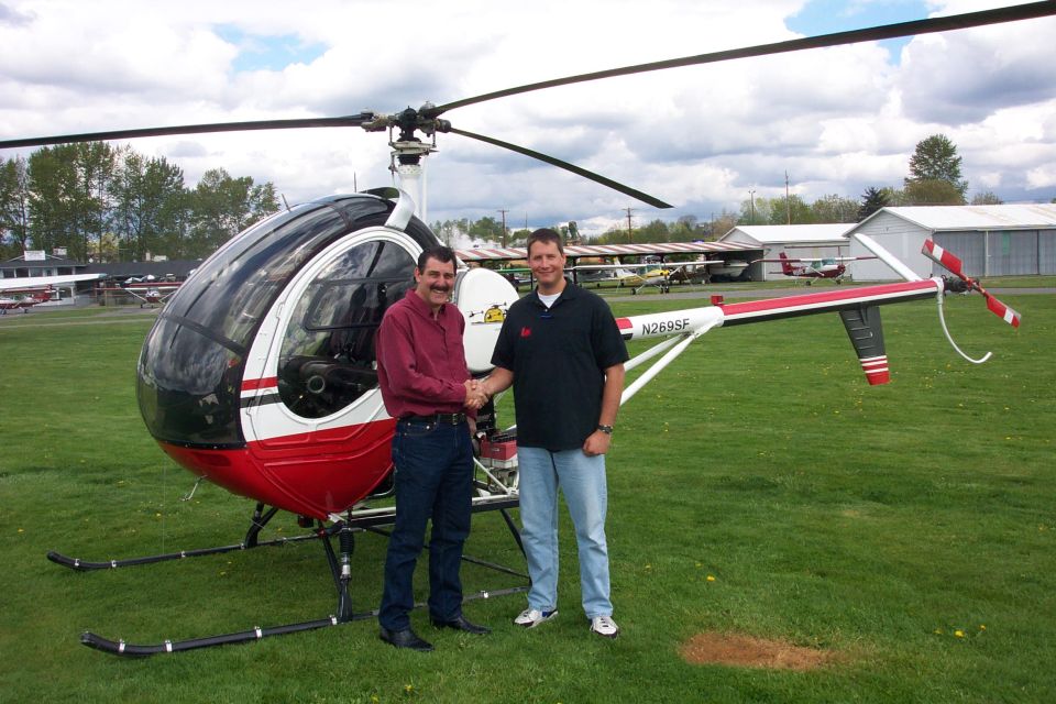 Two men shaking hands beside a red and white small helicopter (N269SF) on grass