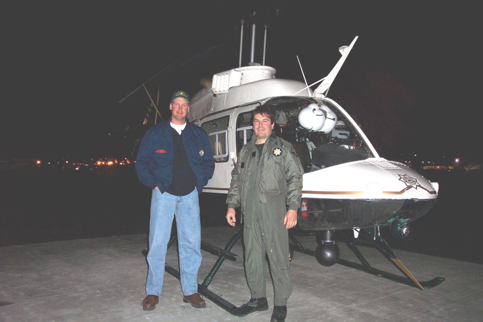 Two men standing in front of a law enforcement helicopter at night
