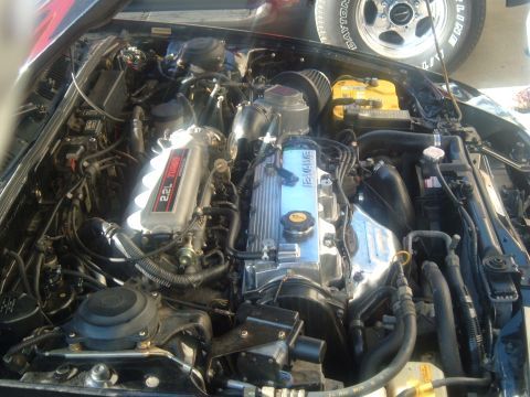1989 Ford Probe - The engine bay of a 1989 Ford Probe features a 2.2L turbo engine with visible modifications and a yellow battery.