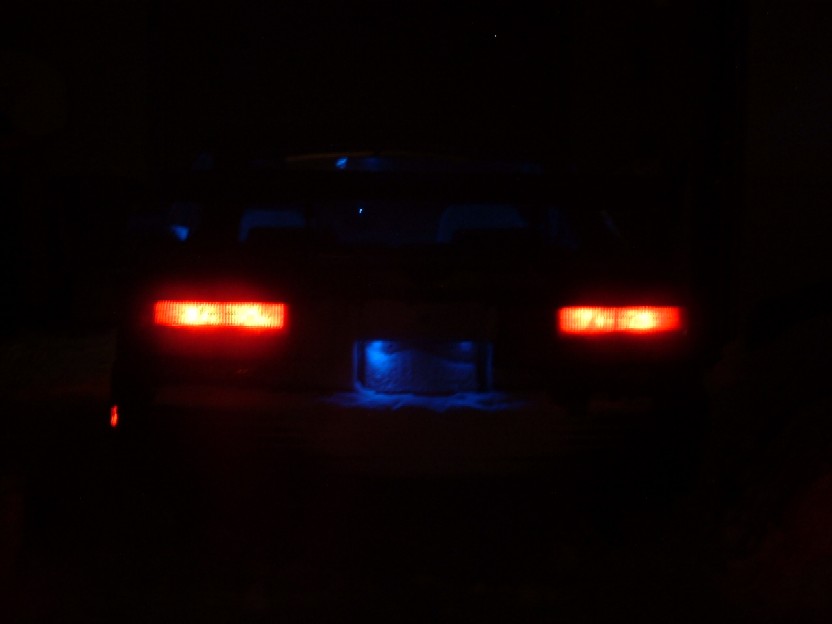 Car rear at night with red taillights and blue underglow. The license plate area is illuminated blue
