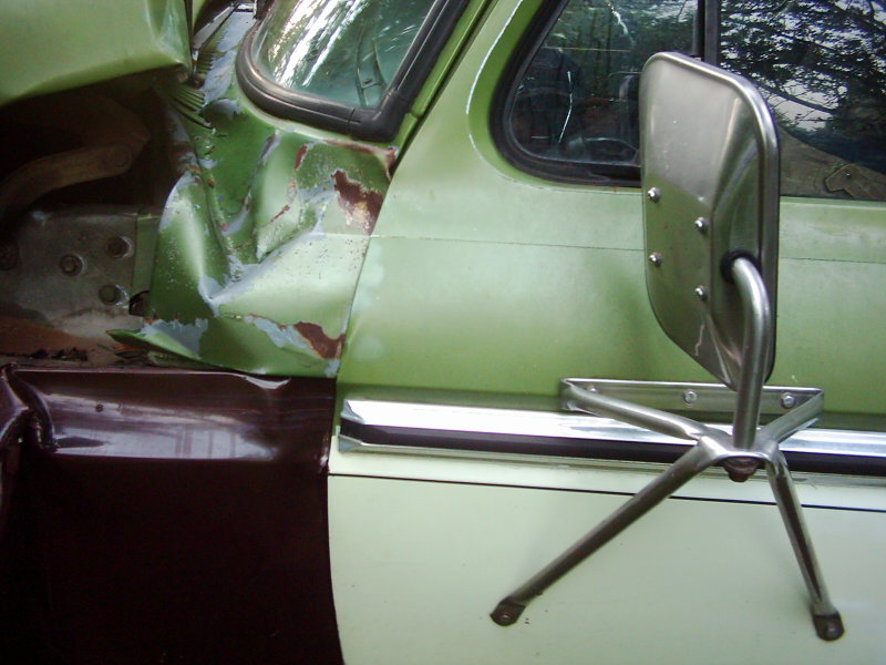 Green and brown truck side with crumpled fender and door, showing rust and damage