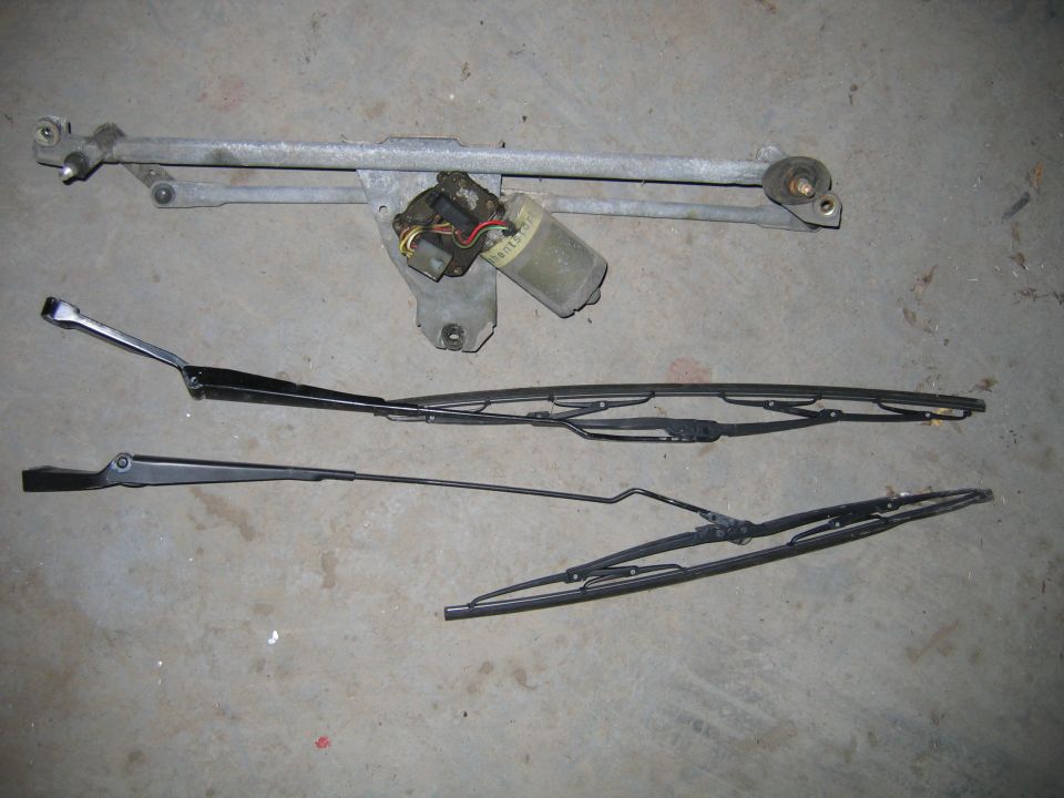 Windshield wiper motor assembly and three wiper blades laid out on a concrete surface