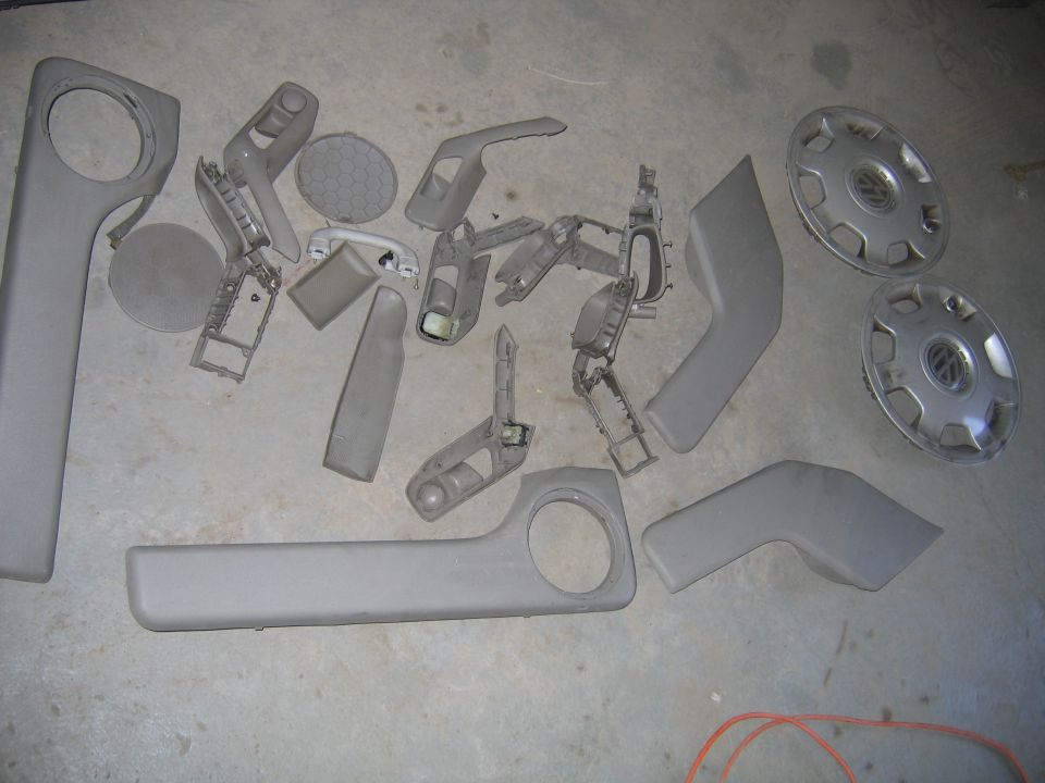 Various gray plastic interior trim pieces and two hubcaps laid out on a concrete floor
