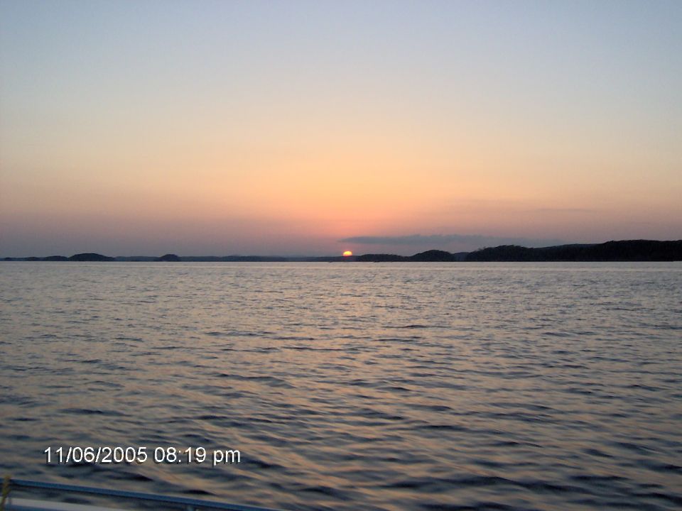 Sunset over a body of water with distant hills, timestamp 11/06/2005 08:19 pm, Supermotors.net logo