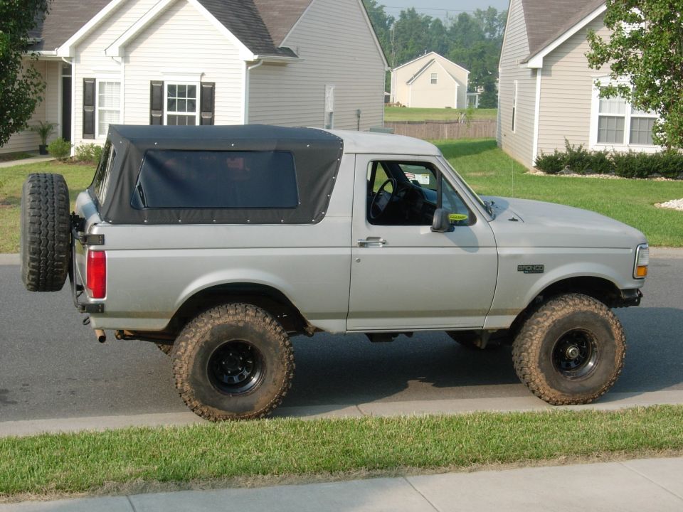 Gray Ford Bronco with black soft top, lift kit and mud tires parked on suburban street