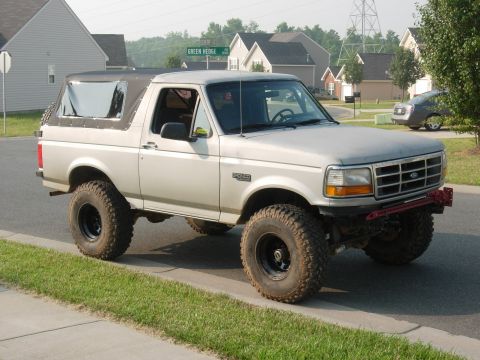 1995 Ford Bronco - A lifted 1995 Ford Bronco with a removable soft top is shown on a suburban street.