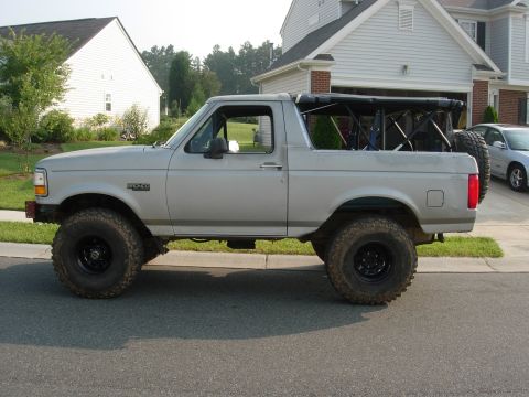 1995 Ford Bronco - Silver Ford Bronco with a soft top and roll cage, lifted suspension, and off-road tires.