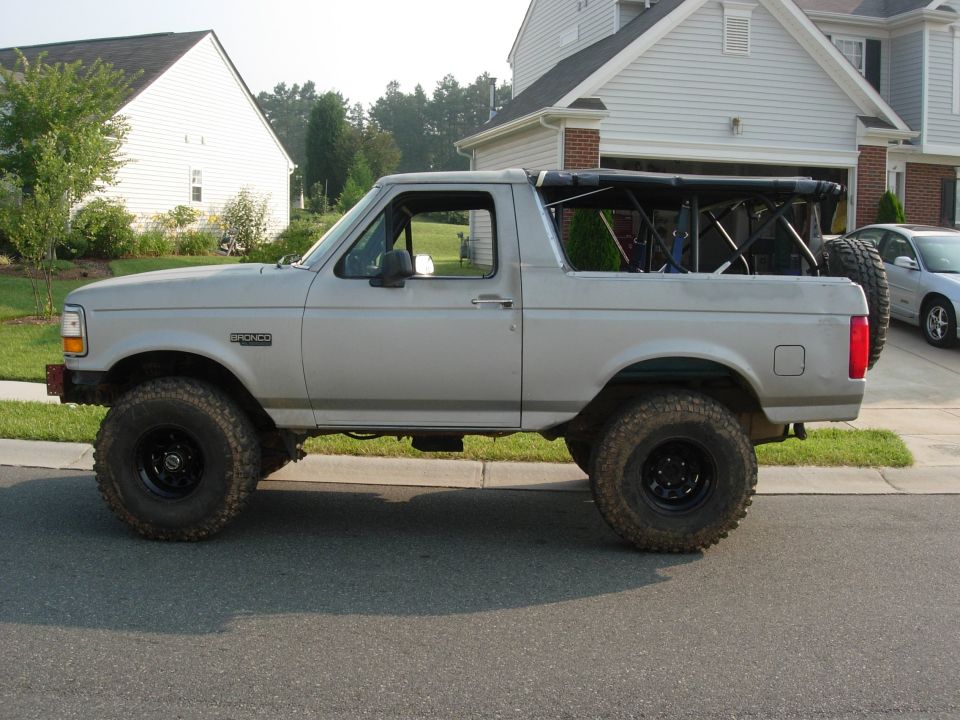 Silver Ford Bronco, side view, top off, lifted on black wheels and mud tires