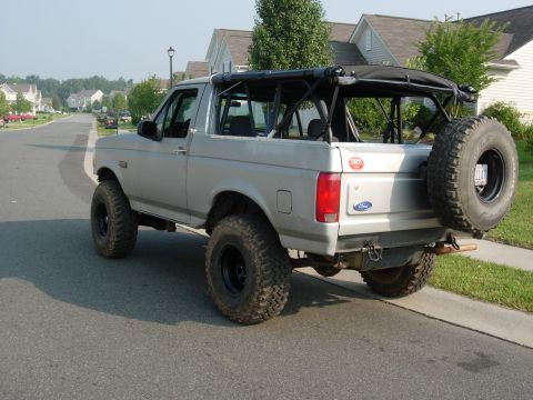 1995 Ford Bronco - This 1995 Ford Bronco features a removable soft top and a rear-mounted spare tire, seen parked on a suburban street.