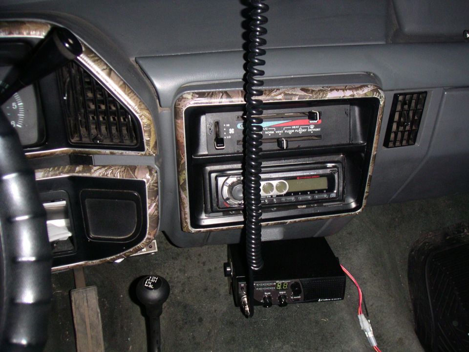 Gray dash of a Ford F-250 with camo trim, aftermarket stereo, Cobra CB radio, and 4x4 transfer case shifter.