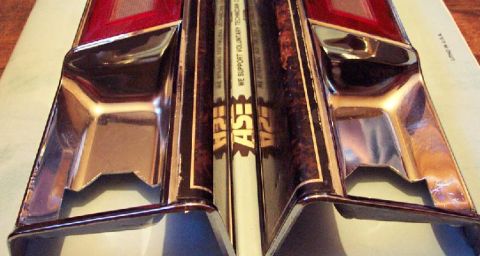 1985 Ford LTD Crown Victoria - Close-up of chrome trim pieces, possibly for a car, resting on top of ASE certification books.