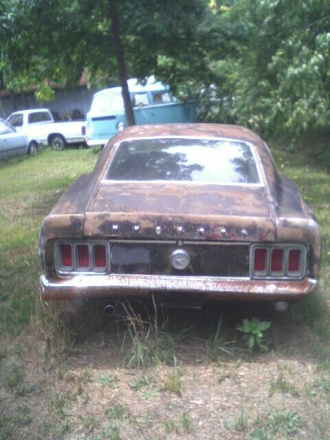 2001 Ford Taurus - Rear view of a weathered 1969 Ford Mustang, showing its iconic triple taillights and chrome bumper.