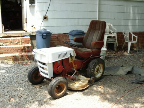 1985 Ford Bronco - A riding lawn mower sits outside a house with trash cans and chairs nearby.