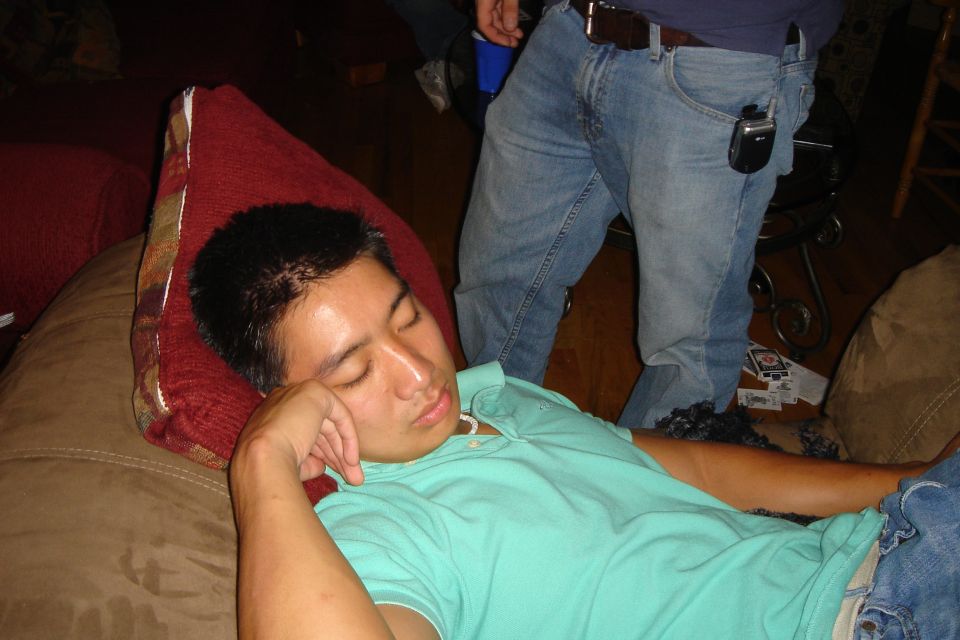 Man sleeping on a brown couch, wearing a teal polo shirt and blue jeans