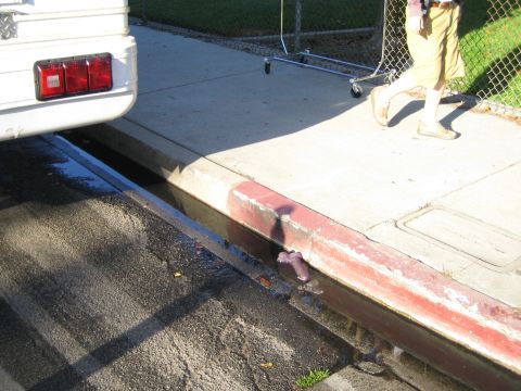 1990 Ford Bronco - taillight corner of a white truck sits on a concrete driveway above a sunken trench, with a person standing on the pavement.