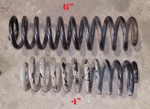 1988 Ford Bronco - Two black coil springs laid side by side on a concrete floor for comparison, labeled with red overlay text reading 6" on the taller top spr…